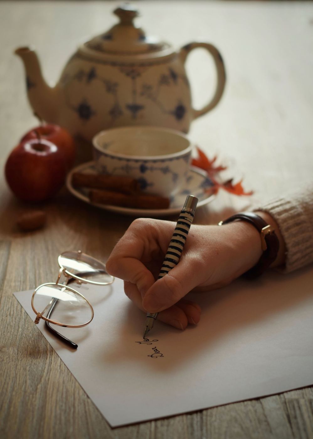 A hand writing a letter with a fountain pen beside a teapot